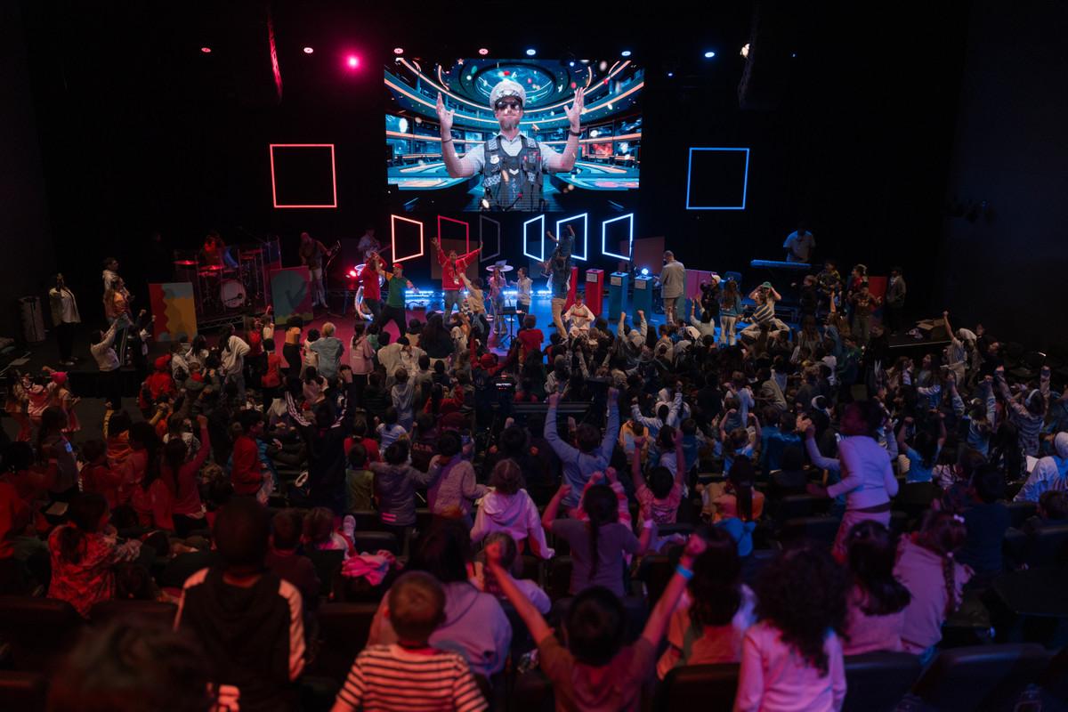 Wide view from behind a seated crowd looking toward a brightly lit kids-event stage.